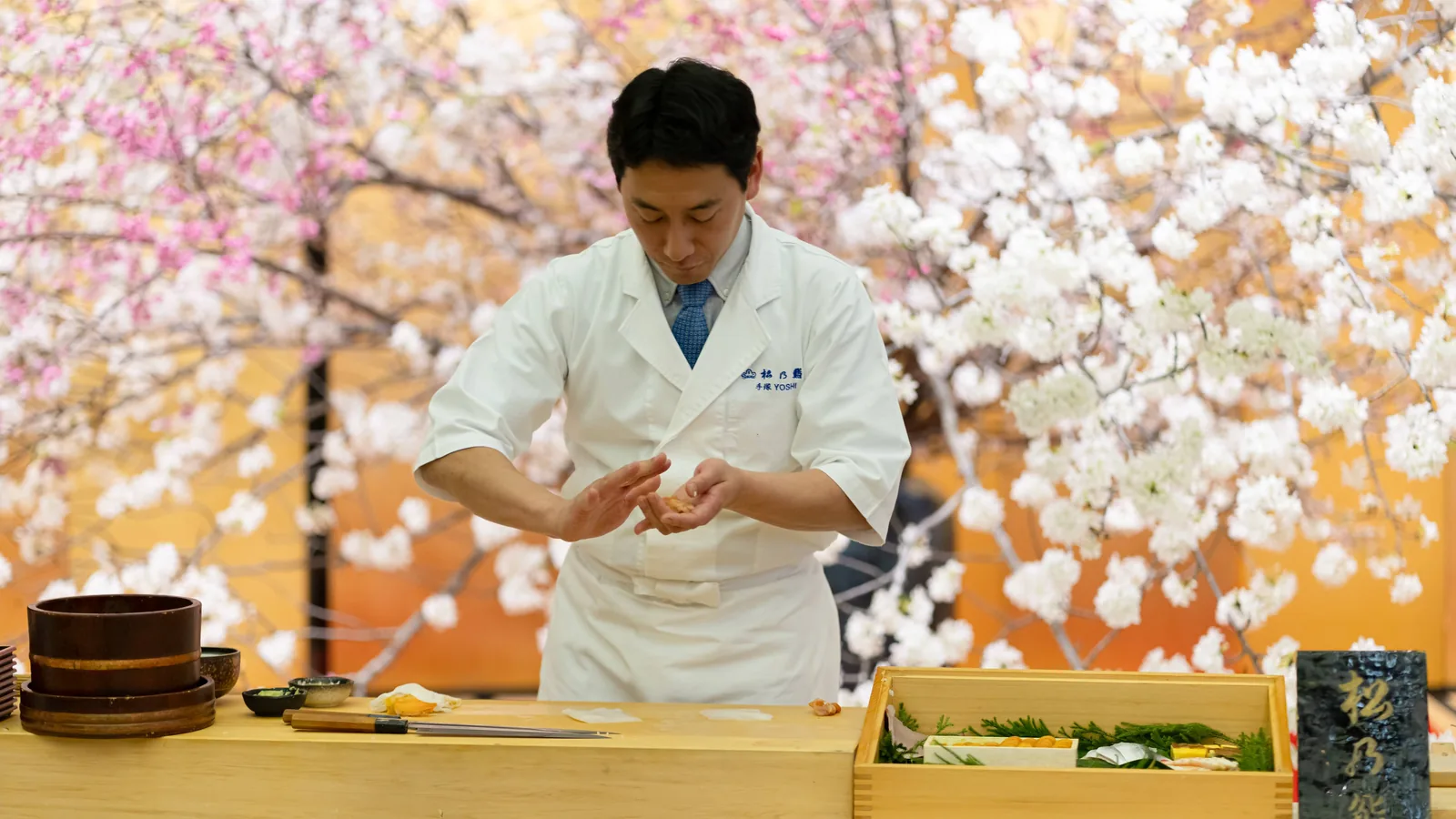 桜の屏風の前で鮨を握る職人